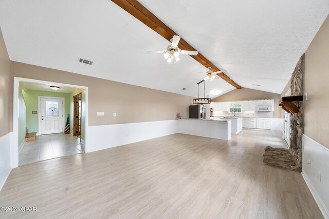 unfurnished living room featuring lofted ceiling with beams, ceiling fan, a stone fireplace, and light wood-type flooring