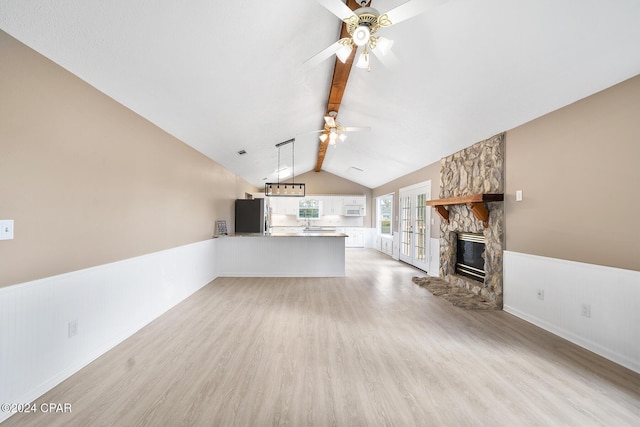 unfurnished living room with ceiling fan, lofted ceiling with beams, a fireplace, and light hardwood / wood-style flooring