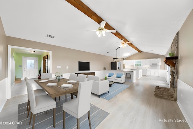 dining room featuring lofted ceiling with beams, light hardwood / wood-style floors, a stone fireplace, and ceiling fan