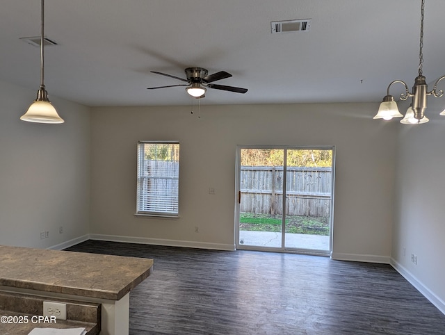 empty room with ceiling fan with notable chandelier, dark hardwood / wood-style flooring, and plenty of natural light