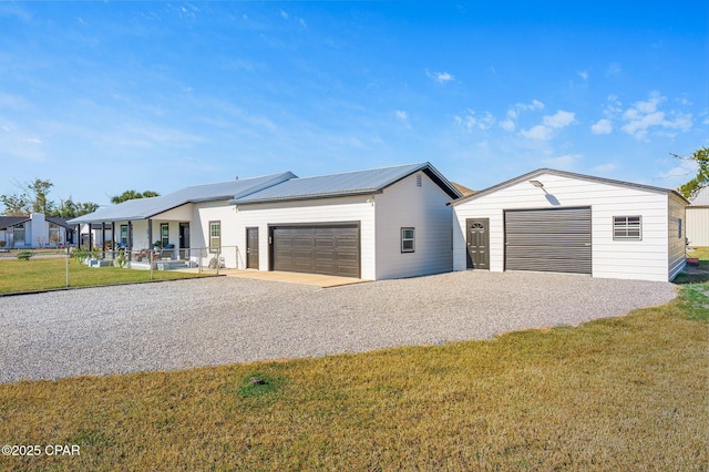 view of front of property featuring a front yard, metal roof, a garage, an outbuilding, and driveway