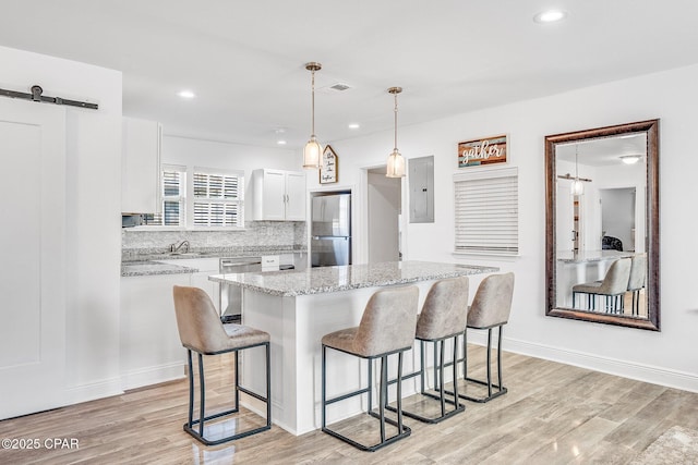 kitchen with pendant lighting, white cabinets, a barn door, a kitchen island, and stainless steel appliances