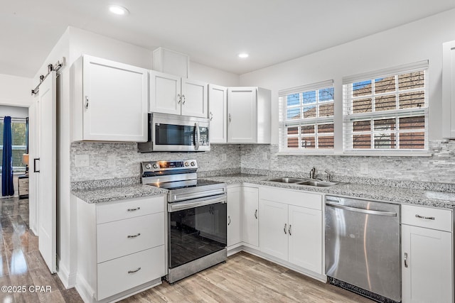 kitchen with appliances with stainless steel finishes, sink, a barn door, light hardwood / wood-style flooring, and white cabinets