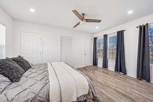 bedroom featuring multiple windows, ceiling fan, light hardwood / wood-style flooring, and two closets