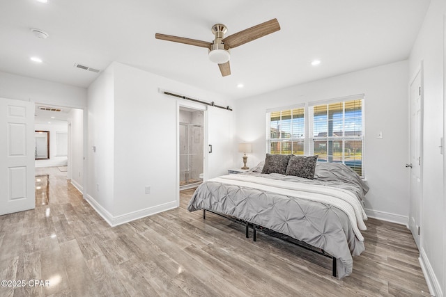 bedroom with a barn door, ensuite bathroom, ceiling fan, and light hardwood / wood-style floors