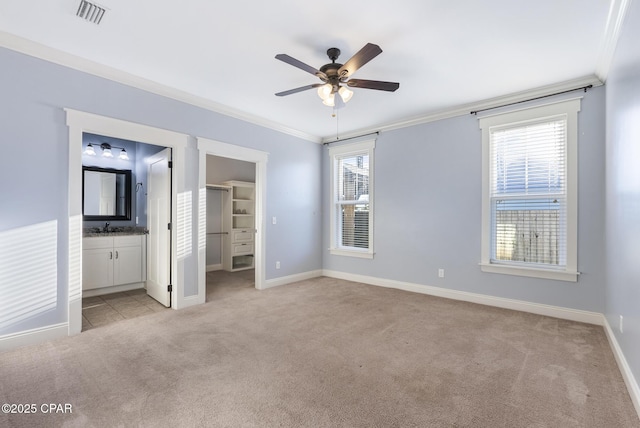 unfurnished bedroom featuring light carpet, a walk in closet, ensuite bathroom, ornamental molding, and ceiling fan