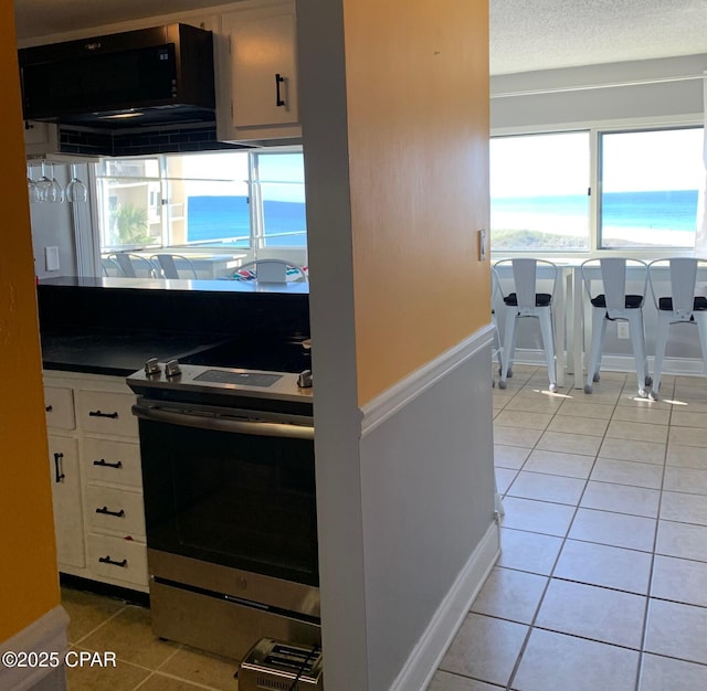 kitchen featuring light tile patterned flooring, stainless steel range oven, a textured ceiling, a water view, and white cabinets