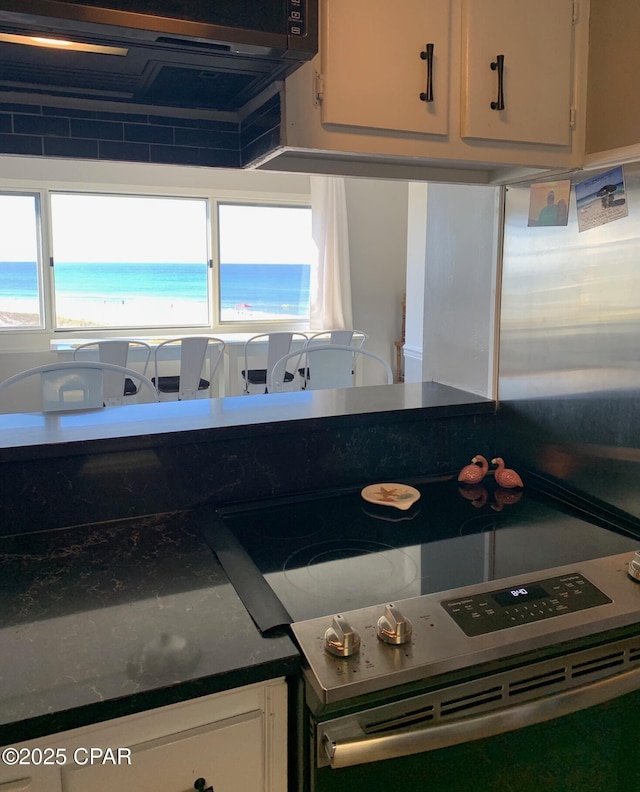 kitchen with white cabinets, a water view, and a view of the beach