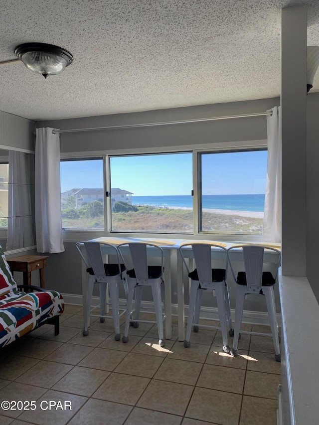 tiled dining room featuring a water view, a textured ceiling, and a view of the beach