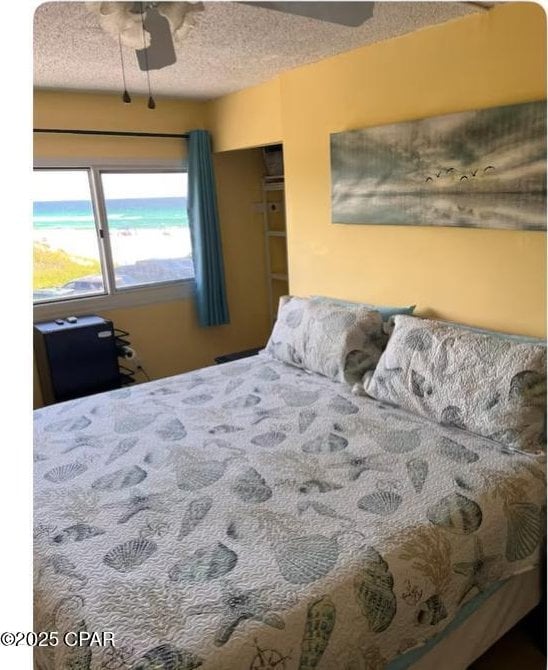 bedroom with a closet, a textured ceiling, a water view, and ceiling fan