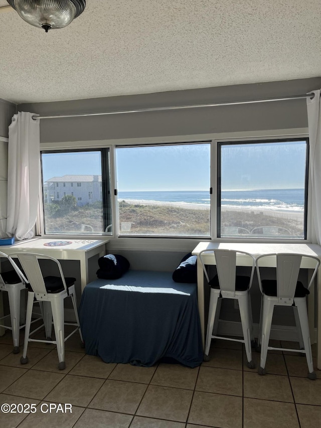 tiled dining area with a water view, a beach view, and a textured ceiling