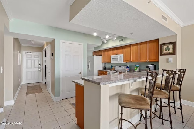 kitchen featuring a kitchen breakfast bar, white appliances, light tile patterned floors, and ornamental molding