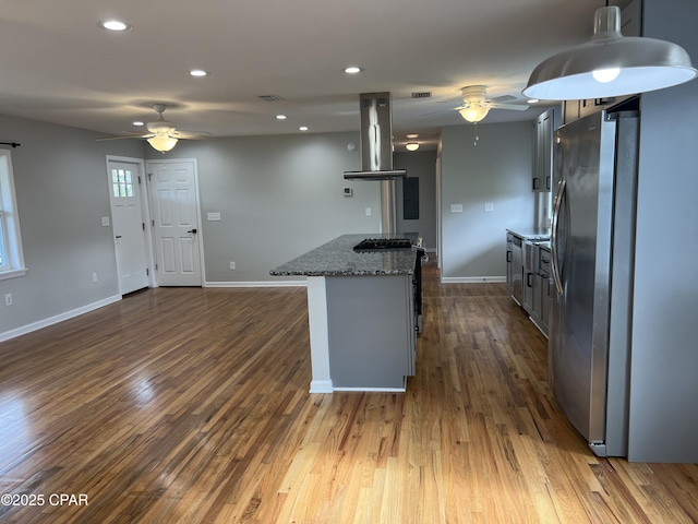 kitchen with island exhaust hood, stainless steel fridge, ceiling fan, dark stone countertops, and hardwood / wood-style floors