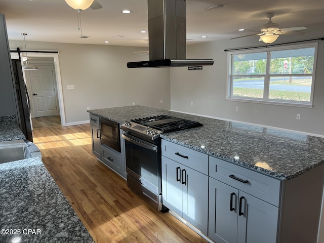 kitchen with island exhaust hood, light wood-type flooring, stainless steel appliances, and dark stone counters