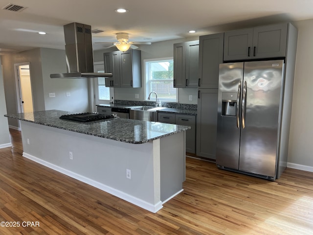 kitchen featuring light hardwood / wood-style floors, island range hood, dark stone counters, and appliances with stainless steel finishes