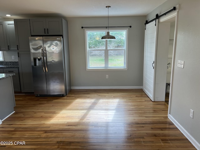 kitchen with gray cabinetry, a barn door, stainless steel refrigerator with ice dispenser, and dark stone counters