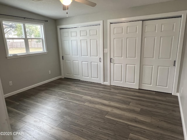 unfurnished bedroom featuring ceiling fan, lofted ceiling, dark wood-type flooring, and multiple closets