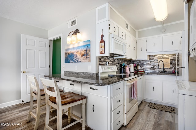 kitchen featuring white cabinetry, sink, light hardwood / wood-style flooring, dark stone counters, and white appliances