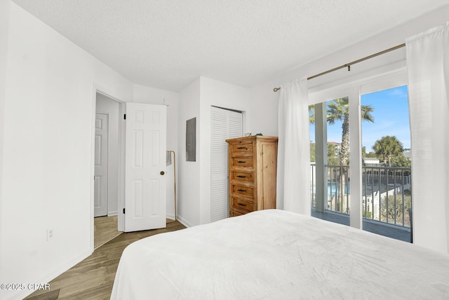 bedroom featuring access to exterior, a textured ceiling, hardwood / wood-style flooring, a water view, and a closet