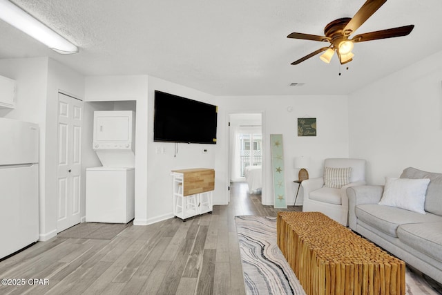 unfurnished living room with ceiling fan, light wood-type flooring, and stacked washer and clothes dryer