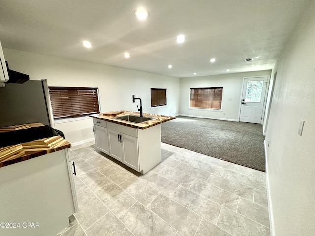 kitchen with white cabinets, light carpet, an island with sink, sink, and stainless steel refrigerator