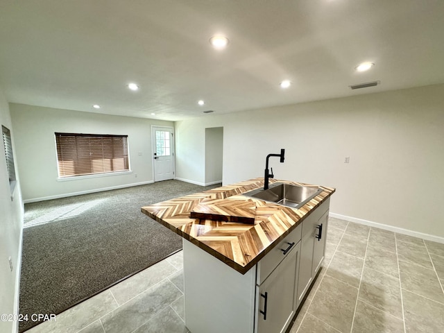 kitchen with light carpet, butcher block counters, gray cabinets, an island with sink, and sink