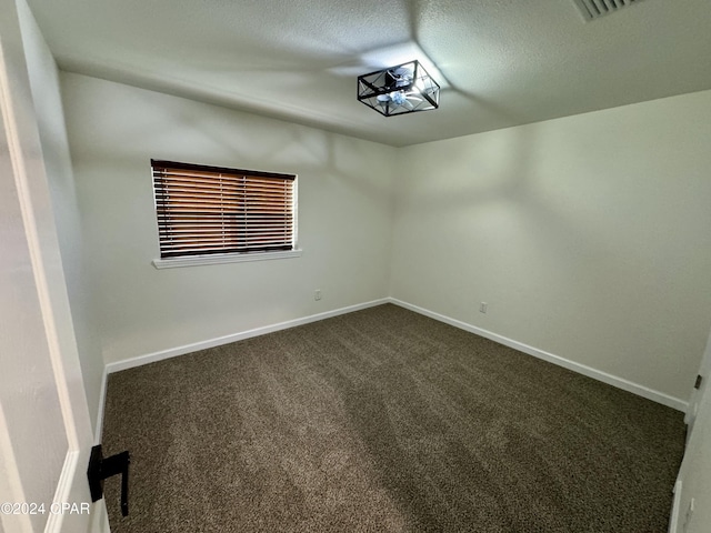 empty room featuring a textured ceiling and dark colored carpet