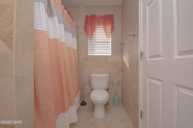 bathroom with a shower with curtain, tile patterned flooring, a textured ceiling, tile walls, and toilet