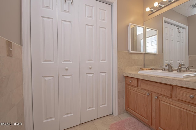 bathroom featuring vanity, visible vents, tile patterned flooring, a closet, and tile walls