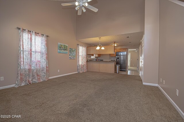 unfurnished living room featuring a towering ceiling, light colored carpet, and ceiling fan