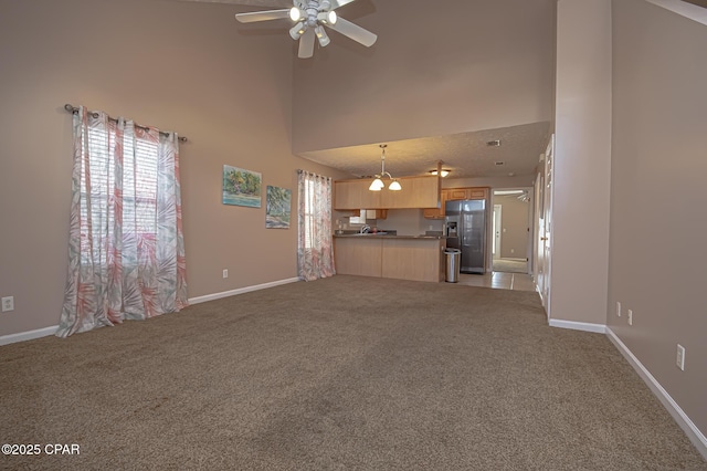 unfurnished living room featuring a ceiling fan, baseboards, a towering ceiling, and light carpet