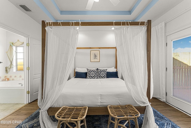 bedroom with access to outside, wood finished floors, a raised ceiling, and visible vents