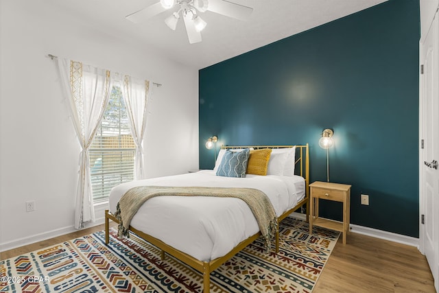 bedroom featuring an accent wall, wood finished floors, a ceiling fan, and baseboards