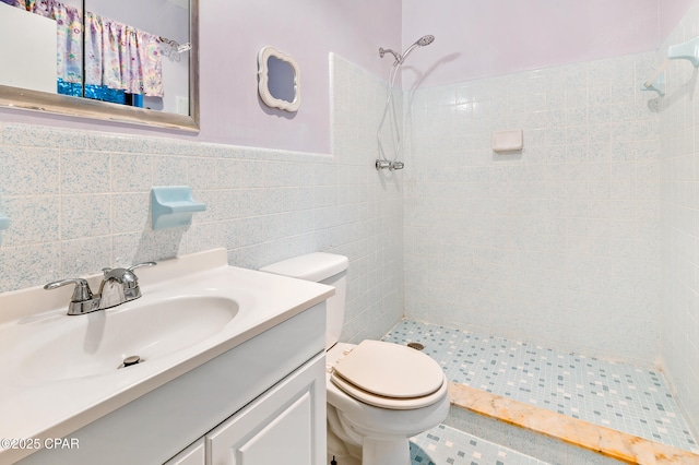 bathroom with a tile shower, vanity, tile walls, and toilet