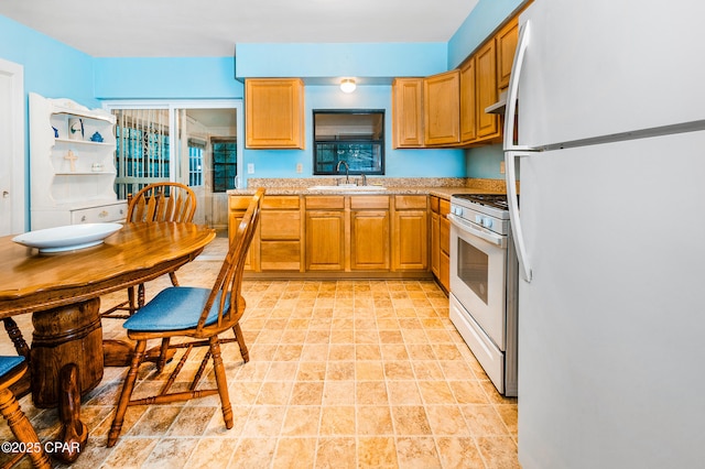 kitchen with under cabinet range hood, light countertops, brown cabinets, white appliances, and a sink