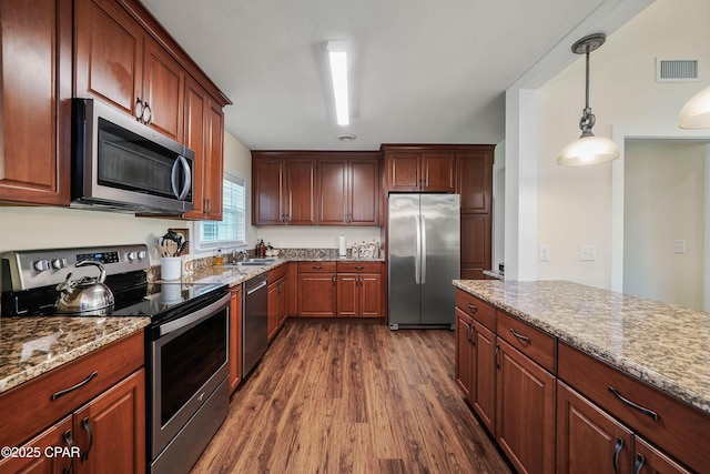 kitchen with pendant lighting, sink, dark wood-type flooring, light stone counters, and stainless steel appliances