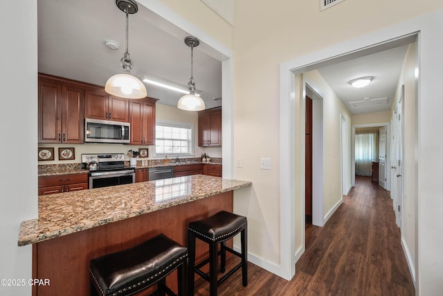 kitchen with appliances with stainless steel finishes, decorative light fixtures, dark wood-type flooring, a kitchen breakfast bar, and kitchen peninsula