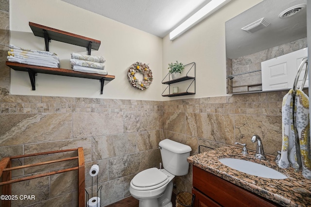 bathroom featuring vanity, toilet, tile walls, and a textured ceiling