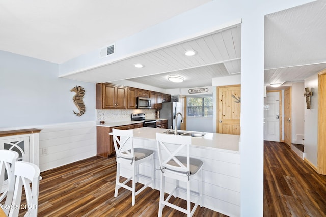 kitchen with stainless steel appliances, tasteful backsplash, sink, dark hardwood / wood-style floors, and a breakfast bar