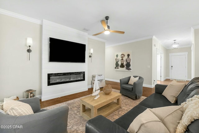 living room with crown molding, a large fireplace, hardwood / wood-style floors, and ceiling fan with notable chandelier