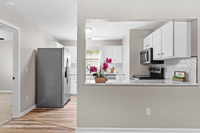 kitchen with stainless steel appliances, light stone counters, kitchen peninsula, decorative backsplash, and white cabinets