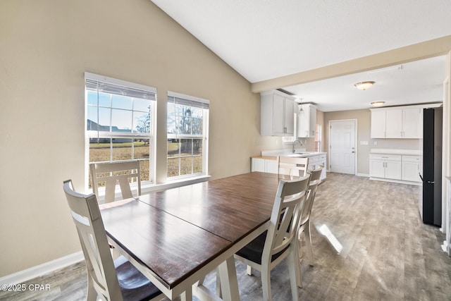 dining space featuring light wood-type flooring, sink, and vaulted ceiling