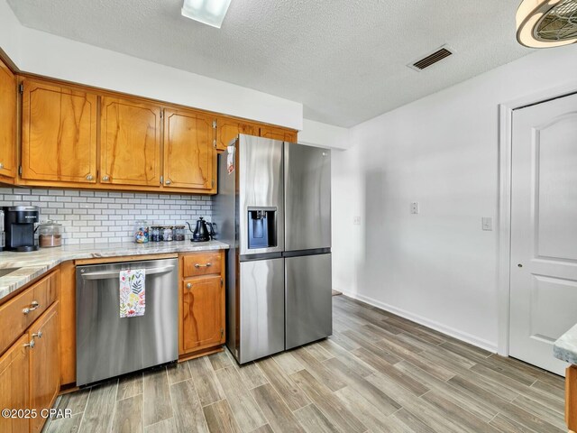 kitchen featuring a textured ceiling, decorative backsplash, appliances with stainless steel finishes, and light hardwood / wood-style floors