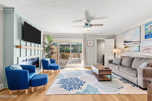 living room with a textured ceiling, light hardwood / wood-style floors, ceiling fan, and crown molding