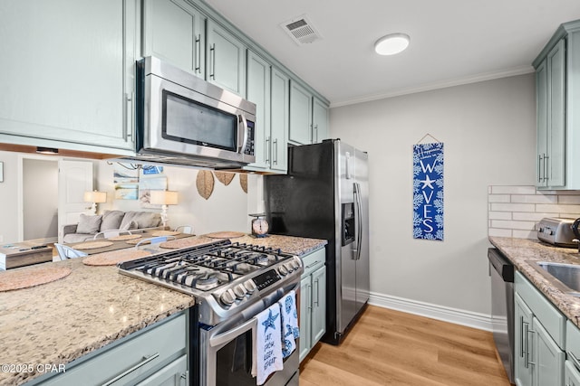 kitchen with light stone countertops, backsplash, crown molding, light hardwood / wood-style floors, and appliances with stainless steel finishes