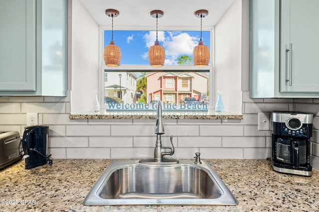 kitchen featuring pendant lighting, light stone counters, sink, and tasteful backsplash