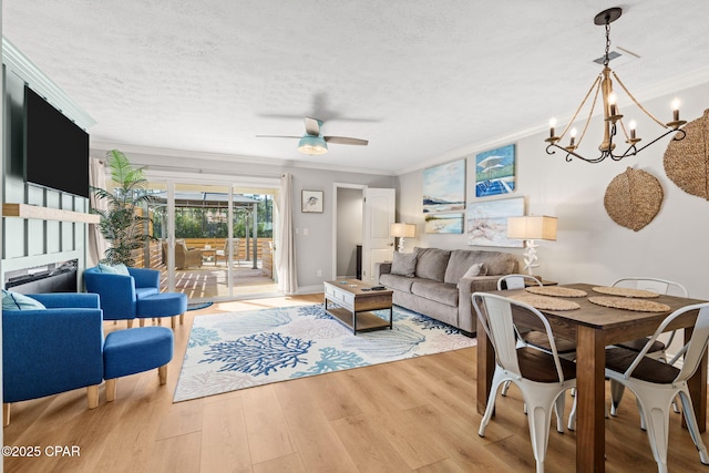 living room featuring light wood-type flooring, a textured ceiling, ceiling fan with notable chandelier, and ornamental molding