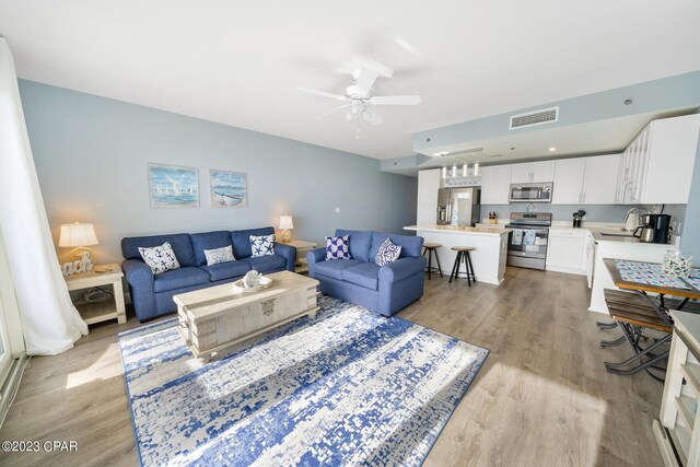 living room featuring ceiling fan, sink, and light hardwood / wood-style floors