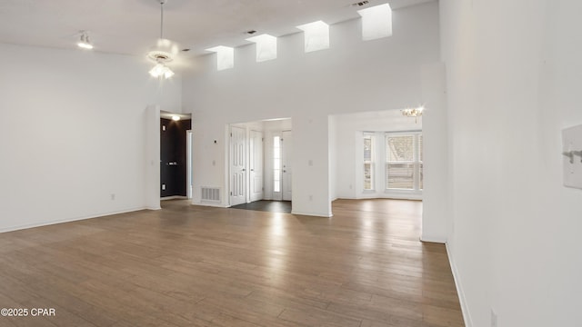 empty room featuring a notable chandelier, wood-type flooring, and a high ceiling