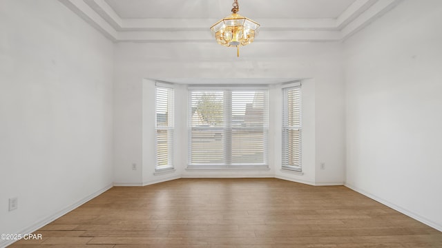 unfurnished room featuring a tray ceiling, wood-type flooring, and an inviting chandelier